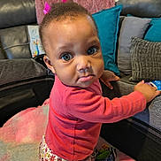 Ruby is registered to the contest to win money with this photo: toddler, child, baby, pink_bow, curious, indoors, playpen, couch, pillows, blanket, patterned_pants, soft_toys, looking_at_camera, face, expression, hand, bright_eyes, clothing, home, floor