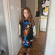 Laura participe au concours pour gagner de l'argent avec cette photo : child, girl, curly_hair, standing, indoor, kitchen, floor_tiles, stitch_clothing, jacket, black_jacket, colorful_dress, footwear, open_toe_shoes, wall, door, refrigerator, papers, magnet, expressionless, person