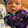 baby, infant, child, portrait, wide_eyed, indoors, sitting, blanket, cushion, colorful_clothing, star_pattern, purple_outfit, brown_hair, blue_eyes, face, eyes, nose, mouth, home, close_up