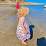 child, toddler, girl, beach, sand, sea, water, shoreline, dress, butterfly_pattern, red_dress, blonde_hair, barefoot, shadow, boat, rock_cliff, reflection, summer, sunlight, playing