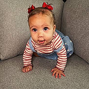 Elora joined the competition — help win amazing prizes! baby, child, crawling, red_bows, striped_shirt, blue_overalls, heart_pattern, gray_couch, indoor, curious, cute, portrait, hands, eyes, clothing, infant, person, home, soft_texture, playful