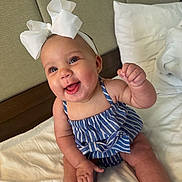 Elora joined the competition — help win amazing prizes! baby, child, smiling, happy, headband, bow, striped_clothing, blue, white, bed, pillow, indoor, cute, portrait, sitting, infant, skin, person, young, cheerful