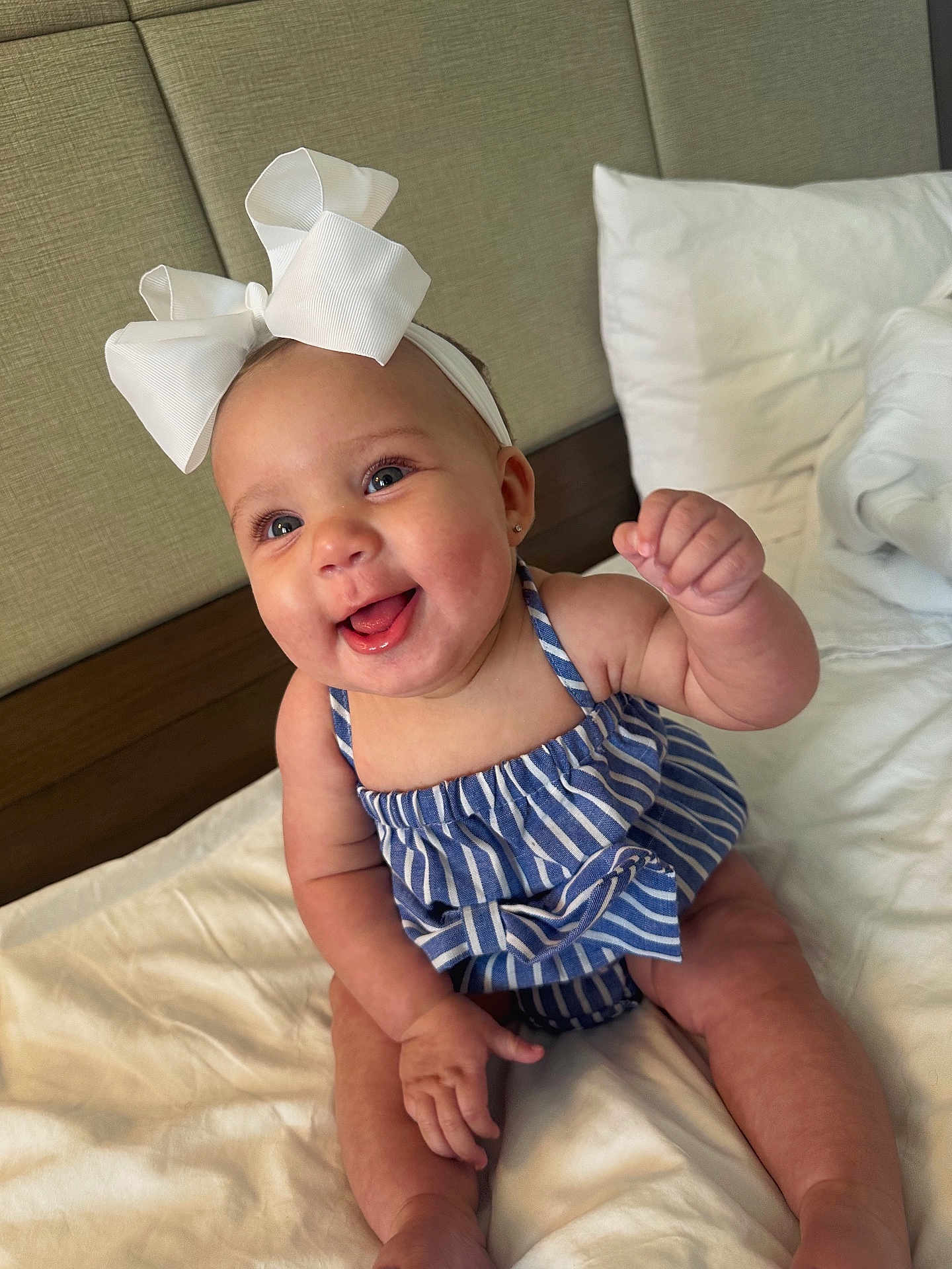 Elora joined the competition — help win amazing prizes! baby, child, smiling, happy, headband, bow, striped_clothing, blue, white, bed, pillow, indoor, cute, portrait, sitting, infant, skin, person, young, cheerful