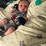baby, infant, blanket, pacifier, mittens, clothing, onesie, person, face, cute, indoor, soft, patterned_blanket, resting, newborn, small, lying_down, cozy, expression, blue_eyes