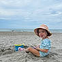 Gabriella joined the competition — help win amazing prizes! child, toddler, beach, sand, bucket, toy, hat, sun_hat, swimsuit, play, water, ocean, sky, cloudy, outdoor, sand_toys, happy, cute, summer, vacation
