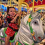 Gabriella is registered to the contest to win money with this photo: child, girl, carousel, horse, amusement_park, ride, polka_dot, red_dress, smile, curly_hair, golden_pole, toy, fun, bright_lights, amusement, entertainment, happy, indoor, people, colorful