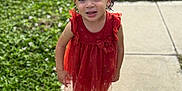 Gabriella is registered to the contest to win money with this photo: child, girl, curly_hair, pigtails, bows, orange_dress, sandals, sidewalk, grass, outdoor, sunlight, smiling, cute, standing, portrait, young, happy, nature, daytime, playful