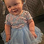 baby, child, blue_dress, flower_crown, smiling, sitting, indoor, quilted_blanket, cute, tutu, infant, headwear, happy, portrait, plush, skin, person, young_child, chubby_cheeks, soft_lighting