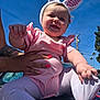 baby, child, pink_clothing, bunny_ears, smiling, outdoor, blue_sky, tattoo, hand, manicure, person, infant, cute, holding, foot, sunny, daylight, happy, playful, portrait