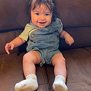 Elijah is registered to the contest to win money with this photo: baby, child, smiling, denim_overalls, socks, couch, happy, indoor, person, cute, toddler, sitting, face, hair, skin, clothing, legs, feet, expression, comfort