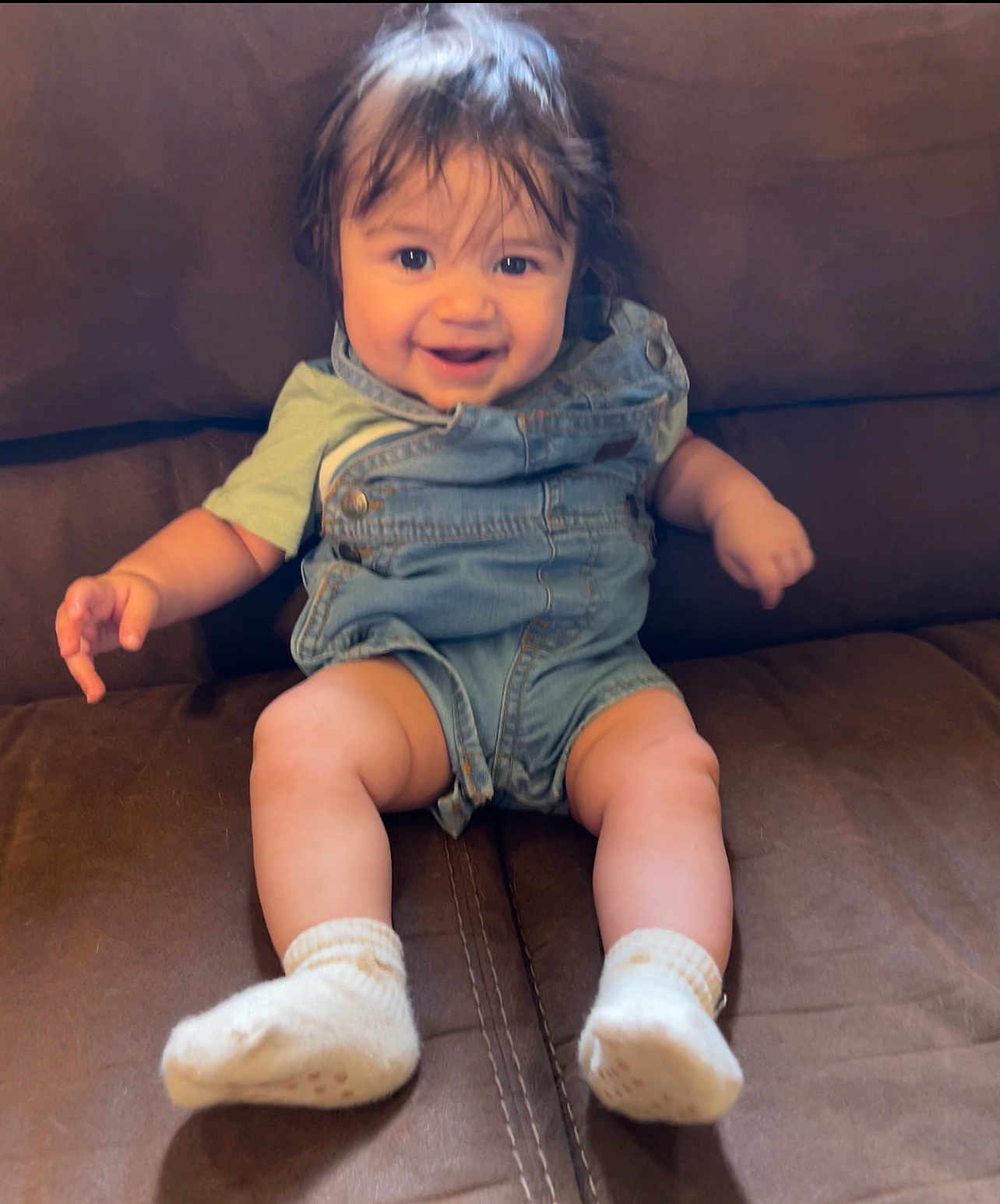 Elijah is registered to the contest to win money with this photo: baby, child, smiling, denim_overalls, socks, couch, happy, indoor, person, cute, toddler, sitting, face, hair, skin, clothing, legs, feet, expression, comfort