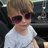 Aaron a rejoint le concours — aidez-le/la à gagner de superbes lots ! child, sunglasses, car_seat, white_tshirt, black_shorts, short_hair, smile, pen_marks, seatbelt, car_interior, window, fence, outdoor, daylight, casual_clothing, boy, portrait, happy, young, cool