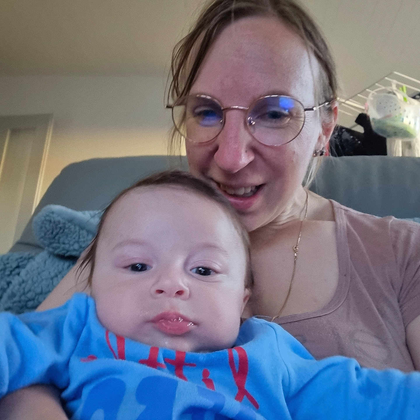 Julie Magnin participe au concours pour gagner de l'argent avec cette photo : adult, baby, blanket, blue_clothing, casual, child, couch, face, furniture, glasses, happy, holding, home, indoor, person, portrait, relaxed, seated, smiling, woman