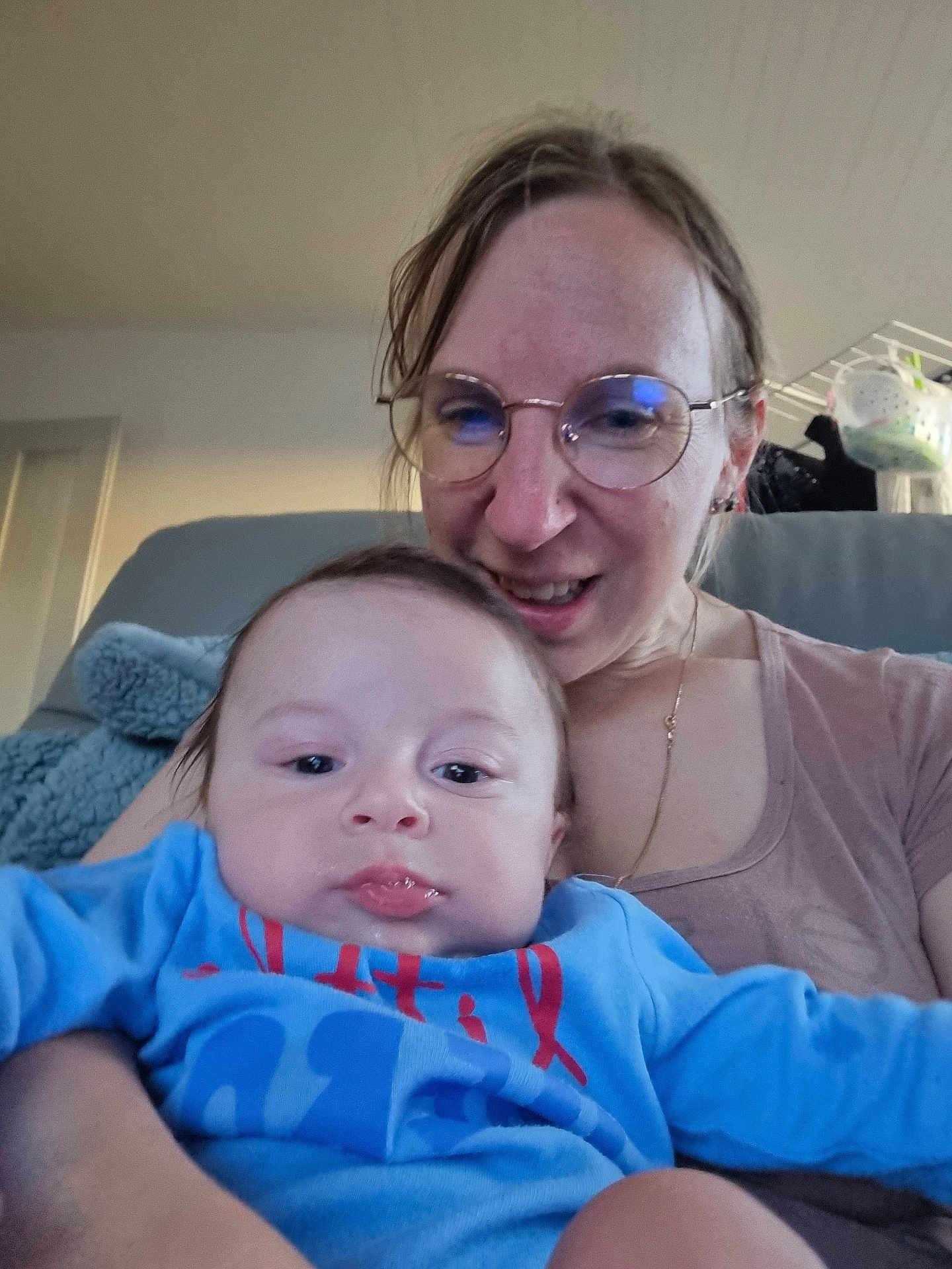 Julie Magnin participe au concours pour gagner de l'argent avec cette photo : baby, woman, glasses, blue_clothing, indoor, smiling, holding, face, person, portrait, casual, furniture, blanket, home, couch, relaxed, child, adult, happy, seated