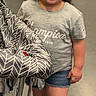 child, girl, smiling, shopping_cart, indoor, gray_tshirt, denim_shorts, brown_sandals, hair_bows, concrete_floor, casual_clothing, happy, standing, person, retail, fashion, portrait, footwear, cute, leisure