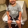 Samira is registered to the contest to win money with this photo: child, girl, smiling, bow, hair_accessory, tshirt, shorts, sandals, pink, gray, chair, medical, examination_room, floor, wooden_floor, curtain, happy, indoors, person, portrait