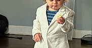 Jaziel joined the competition — help win amazing prizes! toddler, child, curly_hair, white_blazer, navy_shorts, indoor, wooden_floor, window, natural_light, standing, holding_object, curious, young_child, casual_clothing, home_interior, floor, person, portrait, cute, small_object
