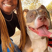 Lola Faílana is registered to the contest to win money with this photo: woman, dog, smiling, braids, cap, outdoor, daylight, happy, tongue_out, pet, animal, casual, nature, trees, concrete, jeans, black_top, sandals, leash, portrait