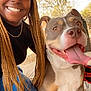 woman, dog, smiling, braids, cap, outdoor, daylight, happy, tongue_out, pet, animal, casual, nature, trees, concrete, jeans, black_top, sandals, leash, portrait