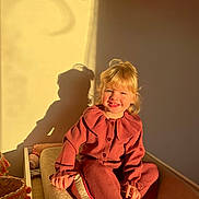 Aleya a rejoint le concours — aidez-le/la à gagner de superbes lots ! basket, blonde_hair, child, cozy, cushion, doll, happy, indoor, knitwear, person, pink_clothing, portrait, relaxed, seated, shadow, smile, sunlight, toy, wall, warm_light