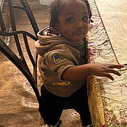 Jaciah is registered to the contest to win money with this photo: child, toddler, smiling, standing, portrait, face, curly_hair, braids, hoodie, sneakers, black_pants, outdoor_style, table, tablecloth, chair, wood_floor, indoor, home, candid, happy