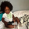 Jaciah joined the competition — help win amazing prizes! child, toddler, baby, portrait, smiling, sitting, bedroom, bed, bedding, controller, gaming, toy, curly_hair, afro_hair, bib, white_shirt, striped_socks, indoors, playful, happy