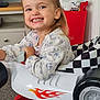 Maisie joined the competition — help win amazing prizes! cabinet, car, carpet, checkered_pattern, child, clothing, face, flame_decal, furniture, hair, happy, indoor, necklace, person, playful, room, smiling, toddler, toy_car, wheel