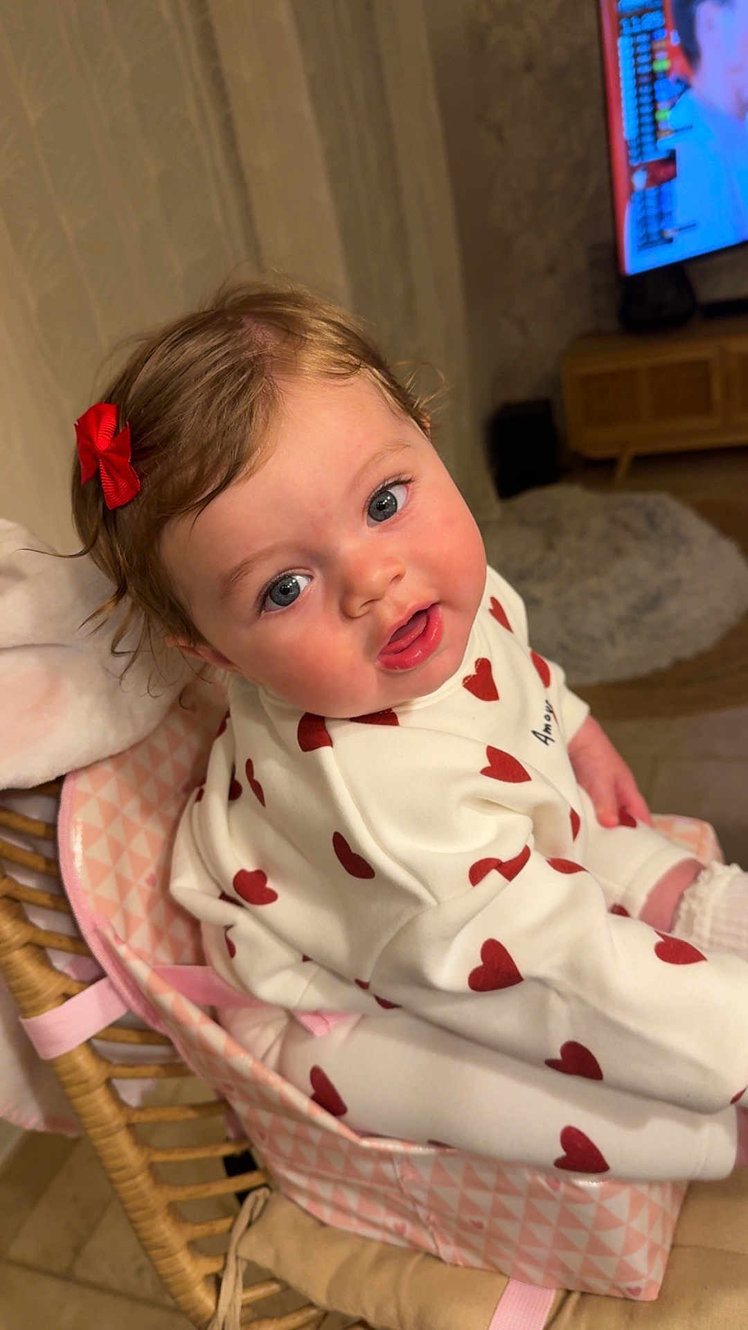 Romy participe au concours pour gagner de l'argent avec cette photo : baby, child, infant, face, blue_eyes, red_bow, heart_pattern, white_outfit, pink_baby_seat, cute, curious, indoors, home, furniture, soft_lighting, sitting, young, person, portrait, adorable