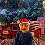 baby, child, santa_hat, christmas_tree, christmas_lights, gift, toy_train, blanket, holiday, festive, smiling, indoors, decorations, red, blue, cute, happy, seasonal, celebration, portrait