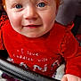 Nova is registered to the contest to win money with this photo: baby, child, red_hair, blue_eyes, smiling, face, hand, blanket, red_shirt, text_on_clothing, indoor, cute, portrait, young_child, infant, seated, holding, cozy, colorful, closeup
