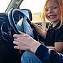 Freya is registered to the contest to win money with this photo: child, smiling, blonde_hair, car_interior, steering_wheel, driving, person, hand, window, beach, seat, clothing, black_shirt, blue_jeans, joy, playful, sunlight, vehicle, passenger, seatbelt