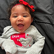 Nala joined the competition — help win amazing prizes! baby, infant, child, portrait, smiling, happy, open_mouth, curly_hair, red_bow, headband, gray_clothing, heart_design, love_message, striped_pants, lying_down, blanket, indoor, close_up, face, adorable