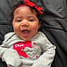 baby, infant, child, portrait, smiling, happy, open_mouth, curly_hair, red_bow, headband, gray_clothing, heart_design, love_message, striped_pants, lying_down, blanket, indoor, close_up, face, adorable