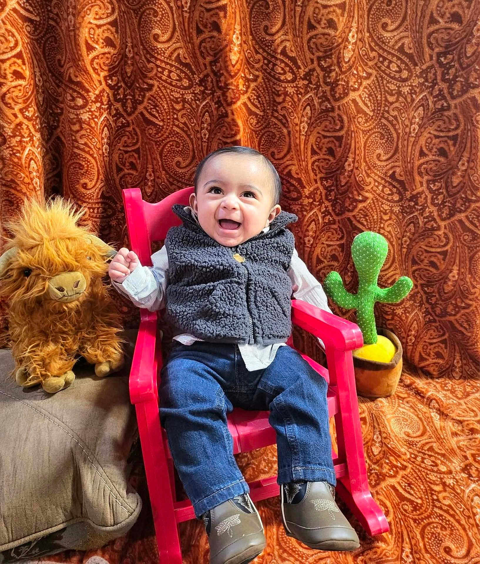 Rey joined the competition — help win amazing prizes! baby, child, smiling, chair, rocking_chair, plush_toy, lion_plush, cactus_plush, clothing, vest, jeans, shoes, indoor, patterned_curtain, happy, portrait, seated, cute, cozy, background