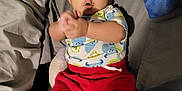 Rey is registered to the contest to win money with this photo: baby, child, clapping, surprised, bed, pillow, blanket, shorts, shirt, monster_print, indoors, cute, expression, person, lying_down, plaid_blanket, footwear_free, skin, infant, happy