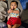 baby, child, clapping, surprised, bed, pillow, blanket, shorts, shirt, monster_print, indoors, cute, expression, person, lying_down, plaid_blanket, footwear_free, skin, infant, happy