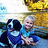 Shiloh is registered to the contest to win money with this photo: dog, child, waterfall, river, rock, blue_bandana, smiling, barefoot, outdoor, nature, autumn, trees, water, happy, sitting, blonde_hair, casual_clothing, daylight, pet, playful