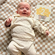 Jeanne participe au concours pour gagner de l'argent avec cette photo : baby, infant, smiling, knitwear, blanket, checkered, card, elephant, milestone, lying_down, cream_color, cute, soft_lighting, indoors, person, portrait, baby_clothes, happy, child, newborn