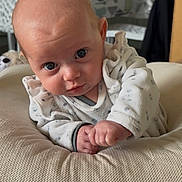 Louise participe au concours pour gagner de l'argent avec cette photo : baby, infant, face, eyes, cushion, clothing, onesie, hand, indoor, person, head, skin, expression, curious, furniture, homedecor, table, kitchen, blurred_background, soft_lighting