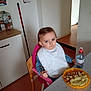 toddler, child, high_chair, bib, spoon, water_bottle, food, plate, kitchen, table, chair, indoor, person, blue_eyes, hair_clip, mashed_potatoes, meal, eating, pink, yellow_plate