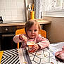 toddler, child, yogurt, spoon, table, chair, kitchen, window, curtain, food, snack, pink_clothing, face, person, indoor, light, furniture, messy, happy, blue_eyes
