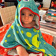 Theo a rejoint le concours — aidez-le/la à gagner de superbes lots ! baby, blanket, child, clothing, curious, dinosaur, face, folded_clothes, furniture, home, hooded_towel, indoor, orange, person, polka_dots, seated, soft_lighting, table, towel, window