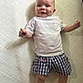 baby, child, smiling, white_tshirt, checkered_shorts, american_flag, lying_down, quilted_surface, dimples, happy, infant, cute, skin, shorts, clothing, person, indoors, young_child, portrait, casual