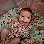 baby, infant, smiling, onesie, floral_pattern, pillow, playpen, pink, happy, cute, lying_down, indoors, child, face, skin, hand, foot, toy, colorful, young