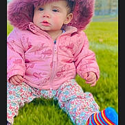 Jesenia Lemus joined the competition — help win amazing prizes! toddler, child, pink_jacket, hood, mouse_ears, grass, outdoor, clouds, sky, colorful_socks, striped_socks, floral_pants, cute, winter_clothing, baby, portrait, sitting, daylight, nature, young_child