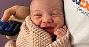 Abigail is registered to the contest to win money with this photo: newborn, baby, infant, smiling, wrapped, blanket, knitted, hand, person, fedex, shirt, phone, holding, portrait, happy, cute, face, indoor, closeup, warm