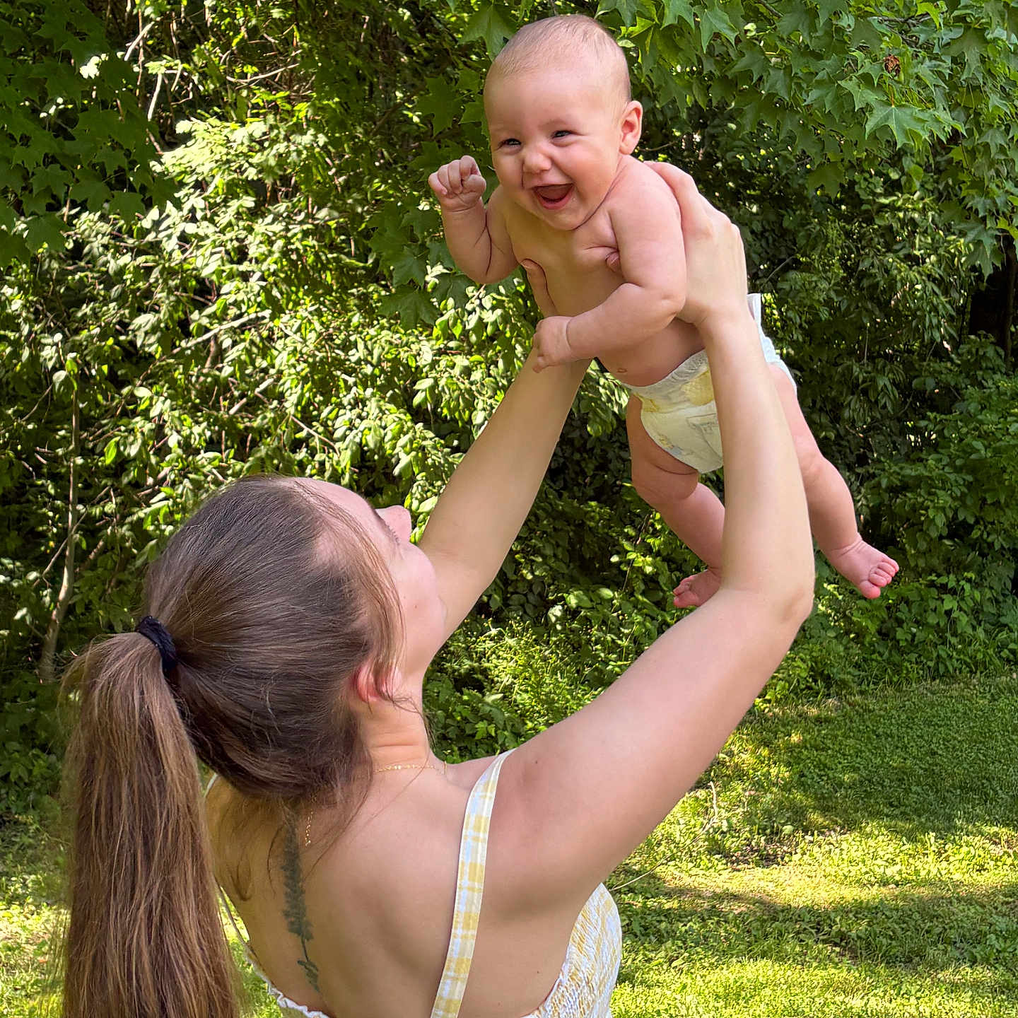Abigail is registered to the contest to win money with this photo: baby, woman, child, outdoor, nature, greenery, trees, grass, sunlight, happy, smiling, holding, playful, summer, dress, long_hair, ponytail, diaper, tattoo, portrait