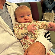 Abigail joined the competition — help win amazing prizes! baby, adult, man, holding, floral_pajamas, indoor, bench, people, woman, hand, face, seated, casual_clothing, public_space, lobby, floor, bag, lighting, portrait, expression