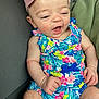 Juniper is registered to the contest to win money with this photo: baby, child, infant, smiling, happy, headband, bow, romper, floral_pattern, colorful_clothing, sitting, fist, skin, person, indoors, fabric, texture, cute, young, portrait