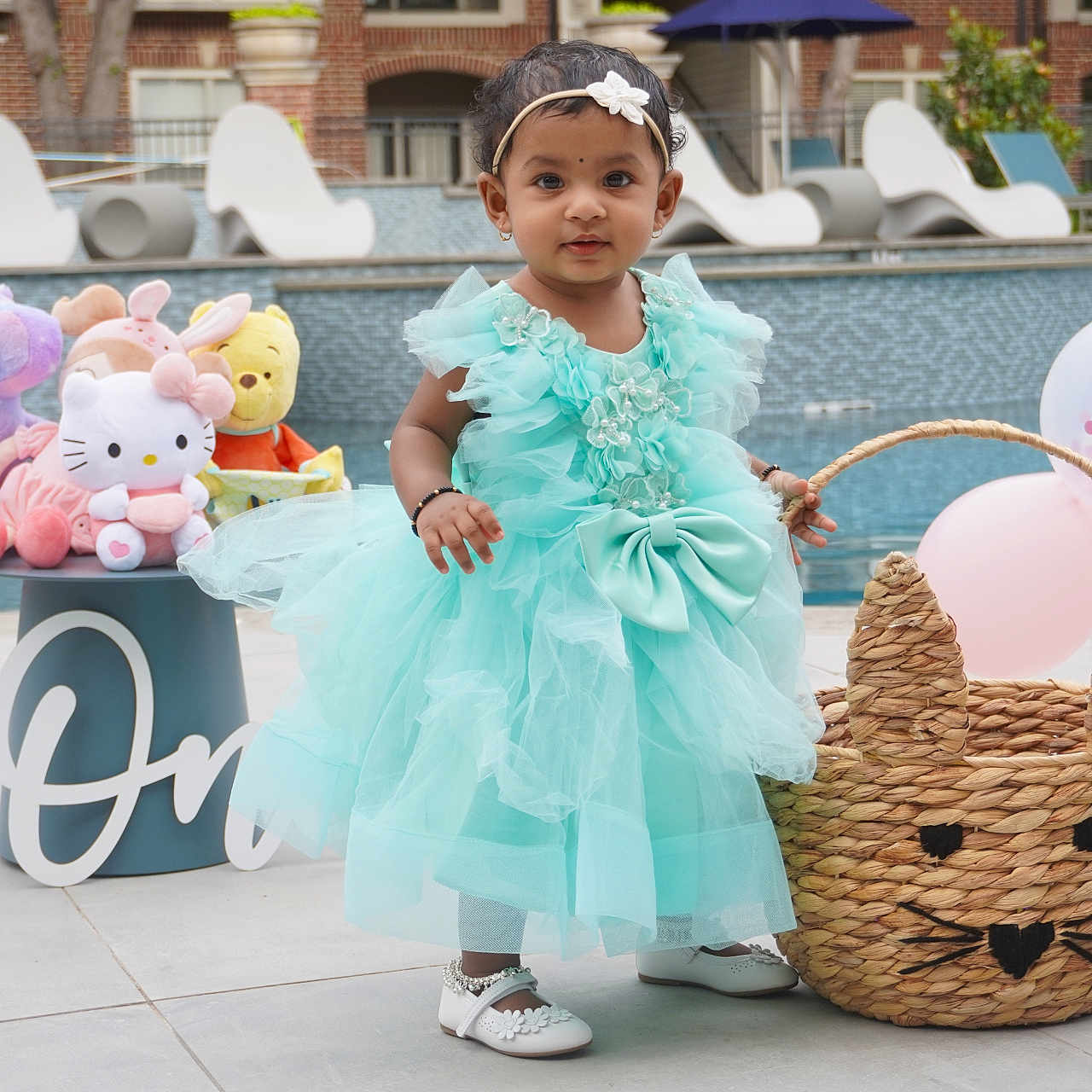 Rutvi is registered to the contest to win money with this photo: balloons, basket, blue_dress, cat_face, celebration, child, concrete_floor, dress, headband, hello_kitty, outdoor, plush_toys, pool, shoes, smiling, table, toddler, unicorn, winnie_the_pooh, woven_basket